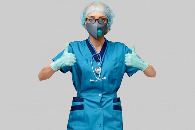 Kobiety lekarka jest ubranym maskę ochronną i lateksowe rękawiczki nad jasnopopielatą ścianą z stetoskopem