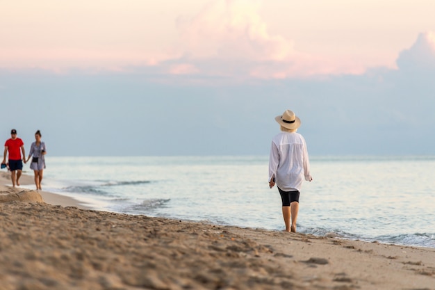 Kobiety mienia telefon komórkowy i być ubranym słomianego kapeluszu odprowadzenie na plaży przy zmierzchem