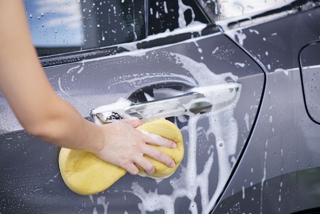 Zdjęcie kobiety myjące samochód z szarym mydłem i żółtą gąbką.