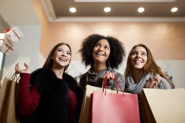 Kobiety o różnym pochodzeniu etnicznym z torbami na zakupy pozują w centrum handlowym na wyprzedaży portret trzech uśmiechniętych