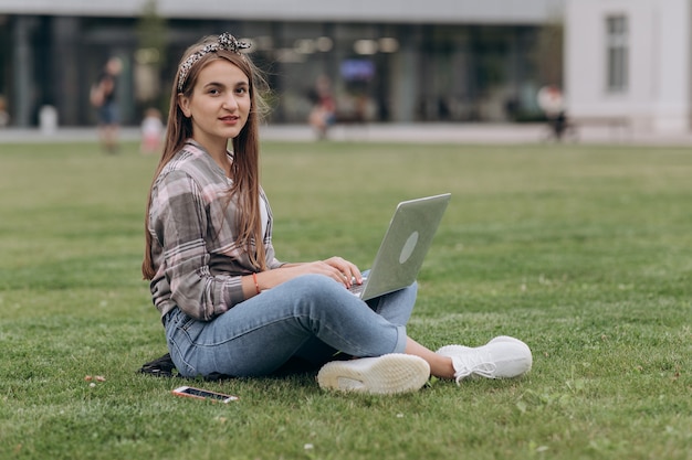 Kobiety obsiadanie na zielonej trawie w parku podczas letniego dnia podczas gdy używać laptop