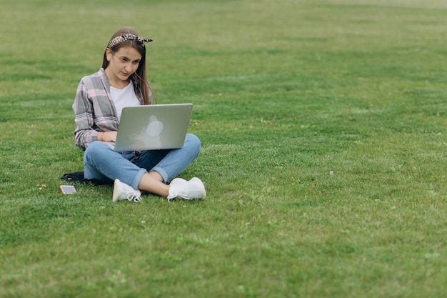 Kobiety obsiadanie na zielonej trawie w parku podczas letniego dnia podczas gdy używać laptop