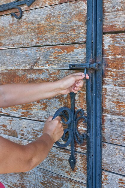 Zdjęcie kobiety otwierają stare drewniane drzwi ozdobione elementami z kutego żelaza.