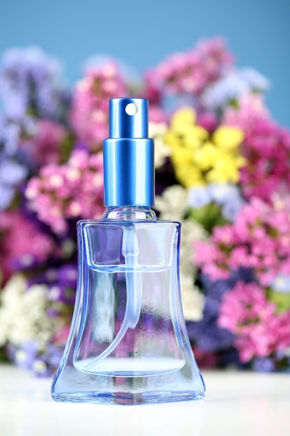 Kobiety perfumy w pięknej butelce i kwiaty na niebieskim tle