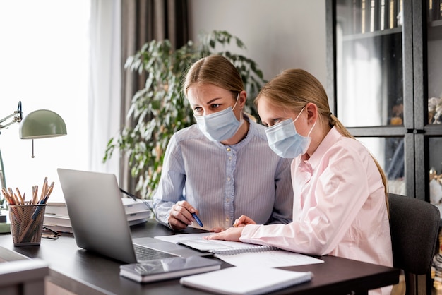 Zdjęcie kobiety pomaga dziewczyna z pracą domową podczas gdy będący ubranym medyczną maskę