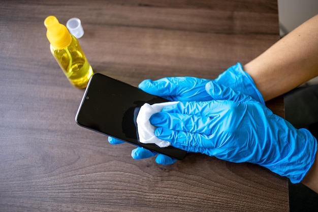 Zdjęcie kobiety przekazują niebieskie rękawiczki do dezynfekcji, czyszczą smartfony, telefony komórkowe mokrymi chusteczkami i alkoholem.