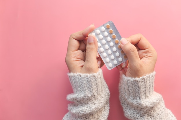 kobiety ręka trzyma pigułki antykoncepcyjne na różowym tle