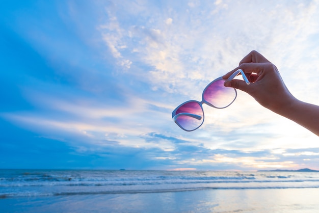 Kobiety ręki mienia okulary przeciwsłoneczni nad morzem podczas zmierzchu