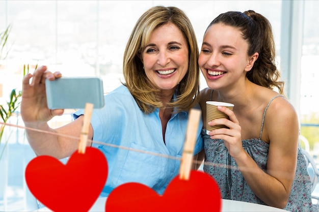 Kobiety robiące selfie telefonem komórkowym na tle czerwonych wiszących serc