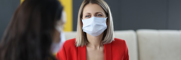 Kobiety w medycznych maskach ochronnych komunikują się w biurze. Bezpieczne miejsce pracy w koncepcji pandemii koronawirusa