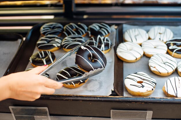 Kobiety wybierające pączki w supermarkecie, szczypce i tacę do bułek