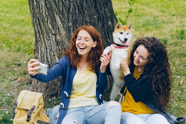 Kochające dziewczyny właścicieli psów robiące selfie ze zwierzakiem w parku za pomocą aparatu w smartfonie
