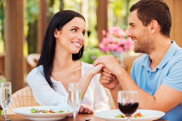 Kocham cię! Piękna młoda kochająca para trzymając się za ręce i patrząc na siebie podczas wspólnego relaksu w restauracji na świeżym powietrzu