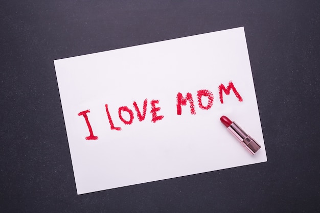 Zdjęcie kocham mamie pisząc od czerwonej szminki w białym papierze na czarnym tle kamienia