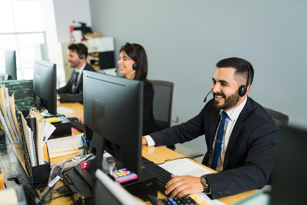 Kochamy naszą pracę w call center. Szczęśliwi współpracownicy siedzący przy biurkach i uśmiechający się podczas pracy jako przedstawiciel handlowy
