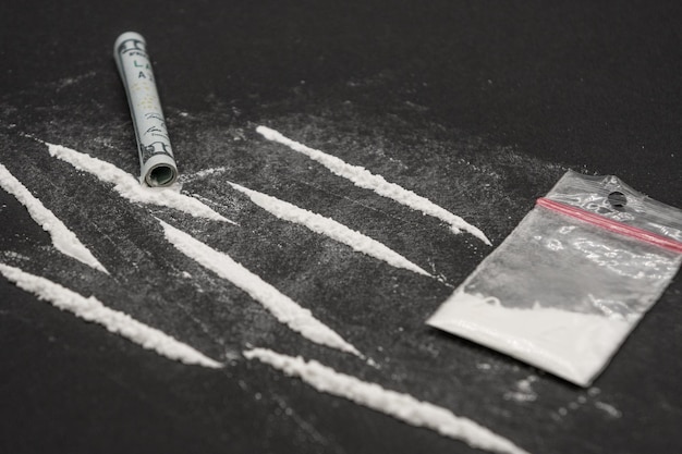Kokaina rozdzielona na ślady na ciemnym stole. Kokaina w plastikowej paczce na czarnym tle.