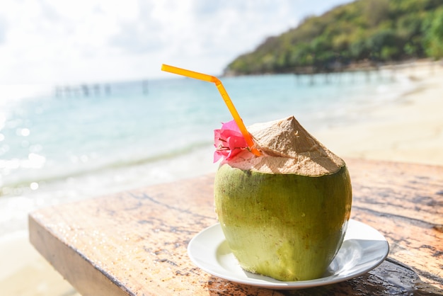 Zdjęcie kokosowe tropikalne owoce na stole i piasek na plaży - świeży sok kokosowy lato z kwiatkiem na plaży morze w upały ocean krajobraz natura wakacje na świeżym powietrzu, młody kokos