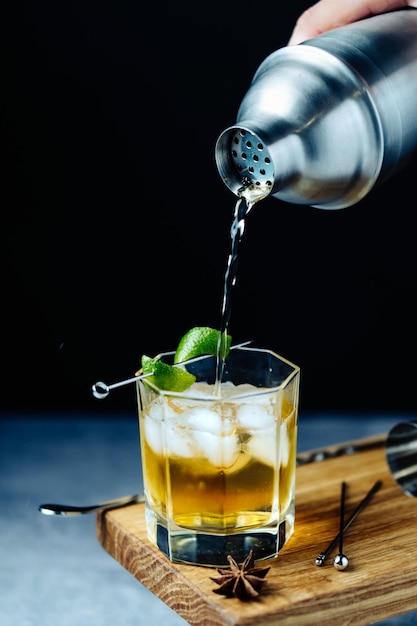 Koktajl alkoholowy przelewający się z shakera do glazury z lodem ze skórki limonki na drewnianym biurku Party time
