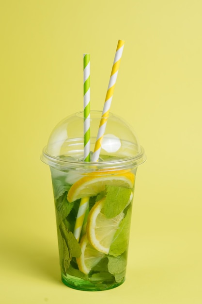 koktajl mojito w plastikowym szkle z rurką na żółtej ścianie yellow