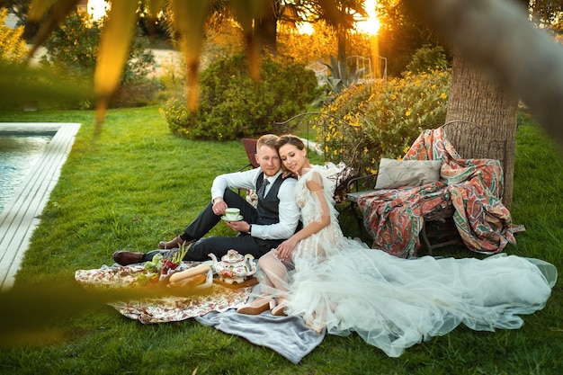 Kolacja nowożeńców na trawniku o zachodzie słońca.Para siedzi i pije herbatę o zachodzie słońca we Francji