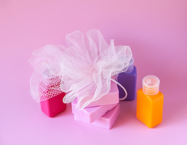 Kolorowa myjka, plastikowe małe butelki podróżne i kostki mydła na delikatnym różowym tle. Zestaw akcesoriów do pielęgnacji i higieny ciała.
