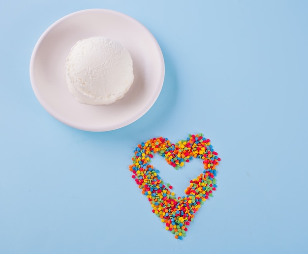 Kolorowe cukierki w kształcie serca i lody na niebieskim tle.