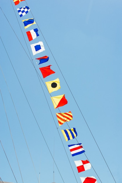 Kolorowe Flagi żeglarskie Pływające Na Wietrze Z Linii Masztu żaglówki Podświetlanej W Błękitne Niebo Przez Słońce.