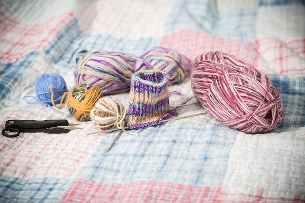 Kolorowe nici, igły i inne przedmioty do ręcznego robienia na drutach na łóżku