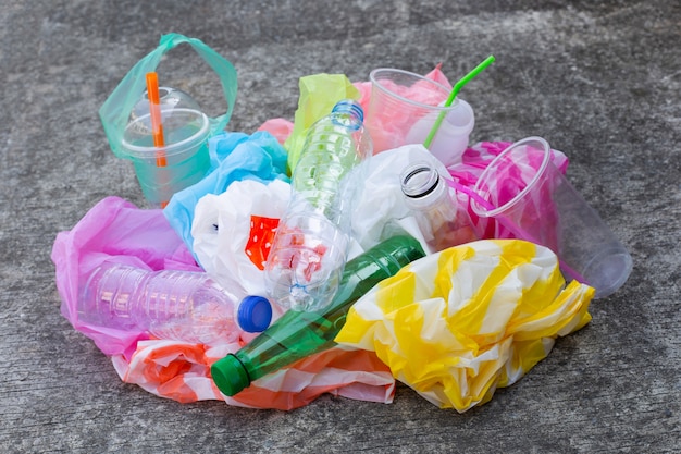 Kolorowe odpady z tworzyw sztucznych, torby, kubki, butelki, słomki na posadzce cementowej