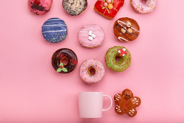 Kolorowe pączki z lukrem i filiżankami kawy na pastelowej różanej powierzchni