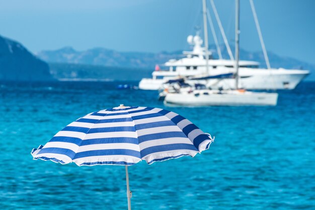 Kolorowe parasole na tropikalnej plaży z błękitnym morzem i jachtami w tle