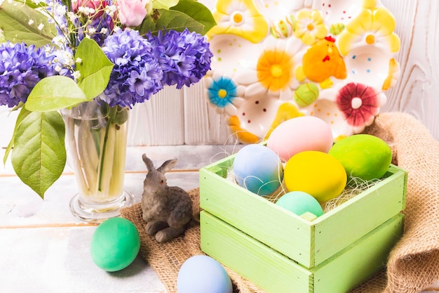 Kolorowe pisanki w zielonym pudełku i figurka królika oraz wiosenny bukiet w wazonie i piękna