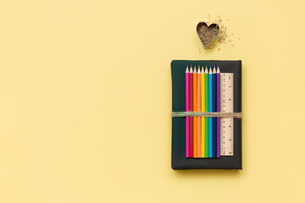 Kolorowe przybory szkolne i biurowe ołówki i linijka na czarnej księdze z wiórami w kształcie serca
