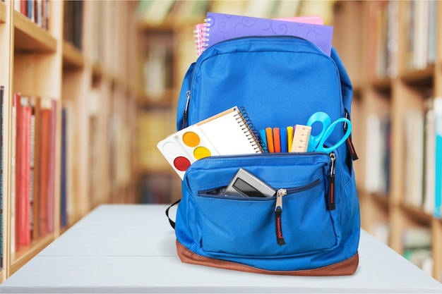 Kolorowe przybory szkolne w plecaku na tle klasy