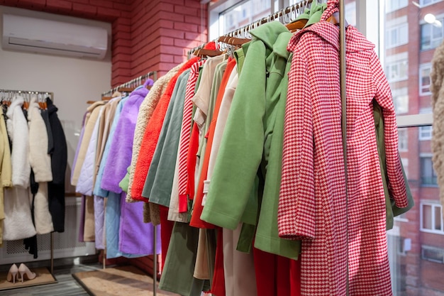 Kolorowe sukienki damskie, kurtki, spodnie i inne ubrania na wieszakach w sklepie detalicznym.
