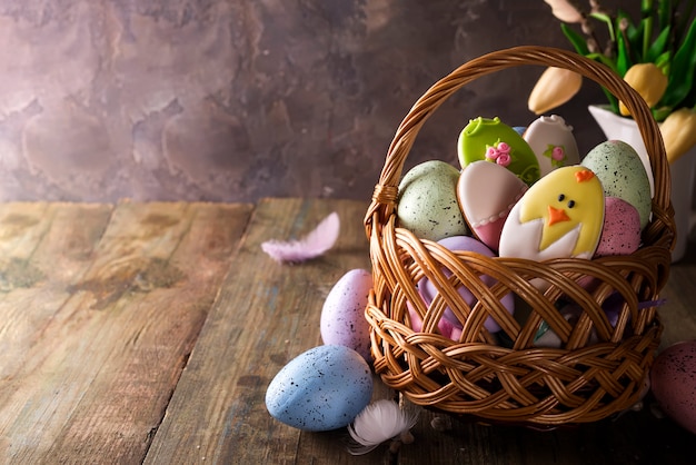 Kolorowi Easter jajka, ciastka w koszu i tulipany kwitną na drewnianym stole.