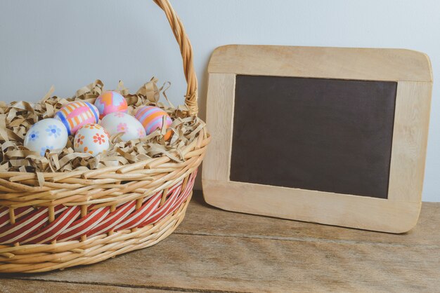 Kolorowi handmade Easter jajka na Słomianym papierze w koszu i chalkboard