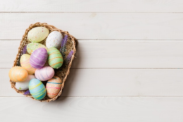 Kolorowi Wielkanocni jajka w łozinowym koszu przeciw kolorowemu tła zbliżenie odgórnemu widokowi z kopii przestrzenią
