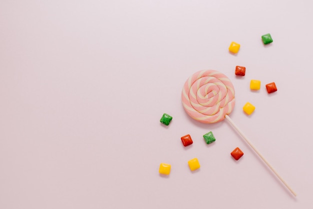 Zdjęcie kolorowy lizak w paski spiralne wielokolorowe cukierki na różowym tle widok z góry