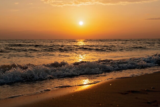 Kolorowy zachód słońca na piaszczystej plaży, fale z pianą na piasku. Ocean, wybrzeże.