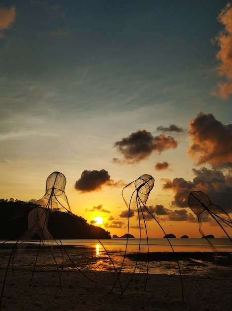 Kolorowy zachód słońca na plaży. Odbicie nieba o zachodzie słońca w wodzie. Sieci rybackie w postaci meduz na plaży