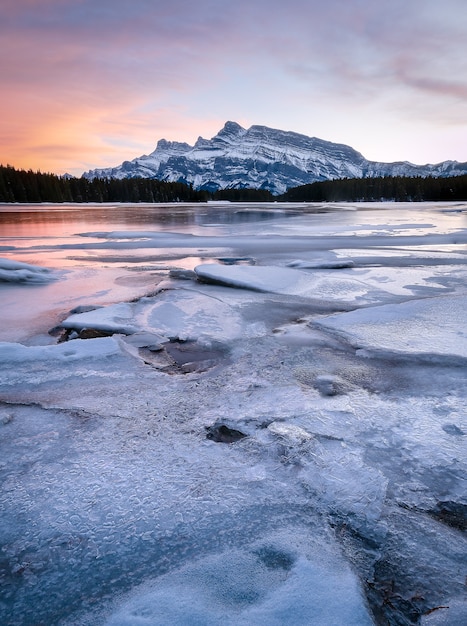 kolorowy zachód słońca nad zamarzniętym jeziorem z dużą górą, zachód słońca nad dwoma jack lake, banff, alberta, canada