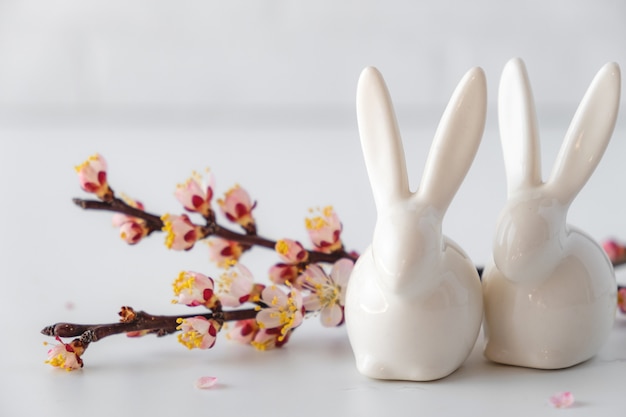 Kompozycja dekoracyjna na wiosnę wielkanocną z białym króliczkiem ceramicznym, różową gałązką wiśni.
