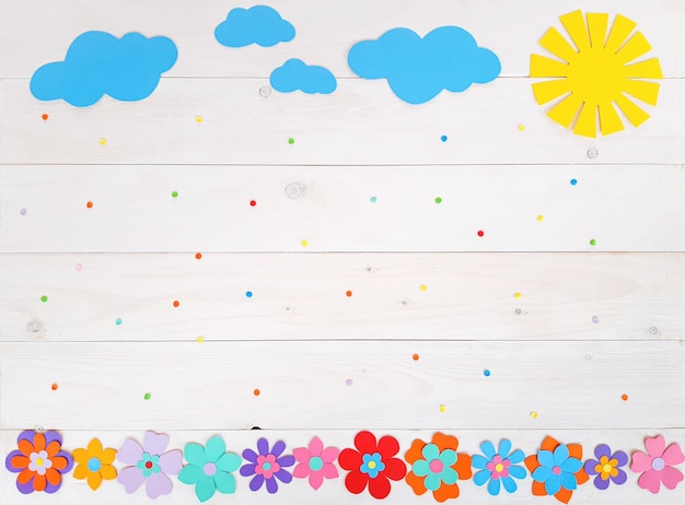 Zdjęcie kompozycja kolorowych letnich kwiatów, słońca, chmurek z wielokolorowego papieru, krok po kroku. dziecko wykonuje rękodzieło własnymi rękami. śliczna kreatywność ręcznie robiona diy na drewnianym stole. widok z góry, kopia miejsca