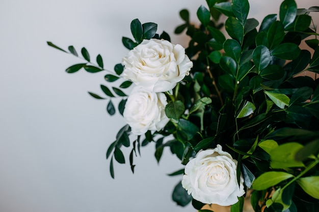 Kompozycja kwiatowa we wnętrzu. Wiązka z białymi różami i zielonymi liśćmi.