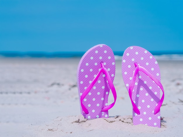 Kompozycja Letnie światło słoneczne. Klapki plażowe na tropikalnym piasku oceanu. przeciw błękitne morze i niebo ściany. Akcesoria plażowe Letnie wakacje koncepcja wakacji na plaży, wycieczka po morzu, ciepłe słoneczne lato