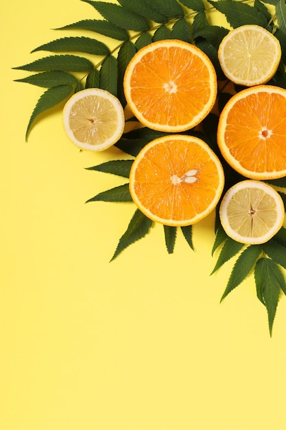 Kompozycja połówek cytryn i pomarańczy z zielonymi liśćmi na jasnożółtej powierzchni, format pionowy