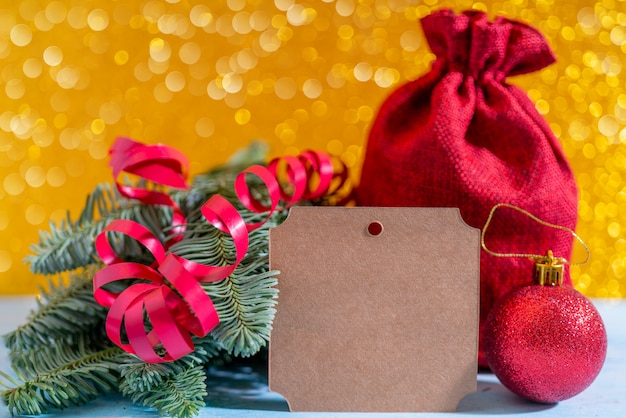 Kompozycja świąteczna na żółto. Gałęzie świerku, torebka z prezentami, czerwona serpentyna i kulki.
