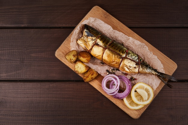 Kompozycja wędzona ryba makrela z ziemniakami udekorowanymi cytryną zieleniną cebulą podawana na drewnianej płycie talerz widok z góry