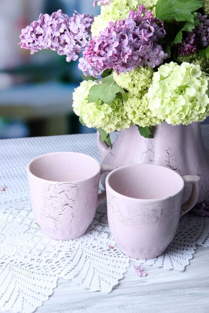 Kompozycja z kubków do herbaty i pięknych wiosennych kwiatów w wazonie, na drewnianym stole, na jasnym tle